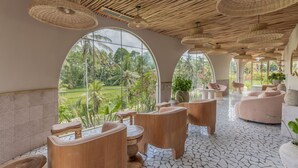 A spacious room with large windows, wooden furniture, and woven ceiling lamps. - Soulshine Bali (Mas)