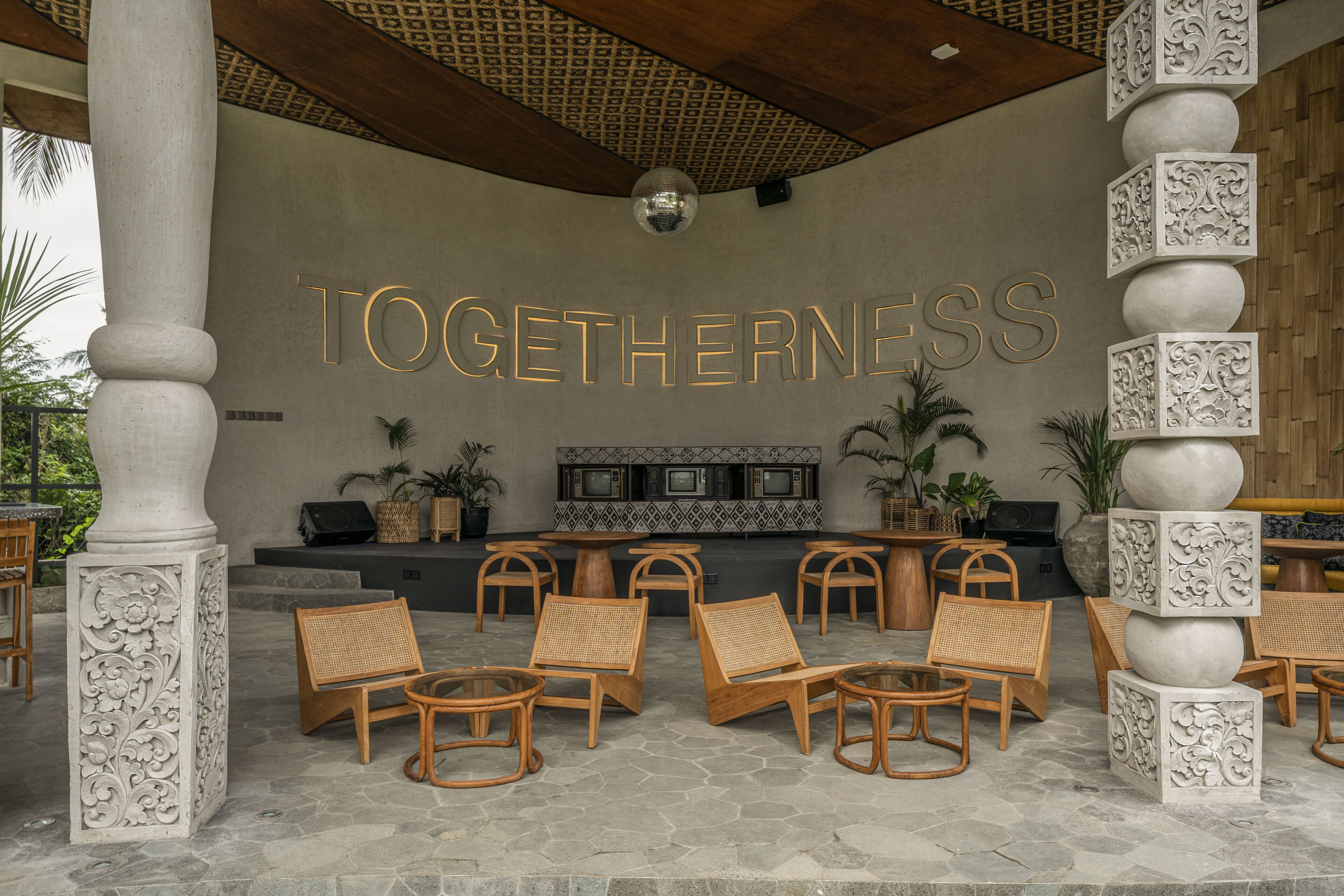 A lounge area with a 'TOGETHERNESS' sign, wicker chairs, a bar area, and decorative columns.