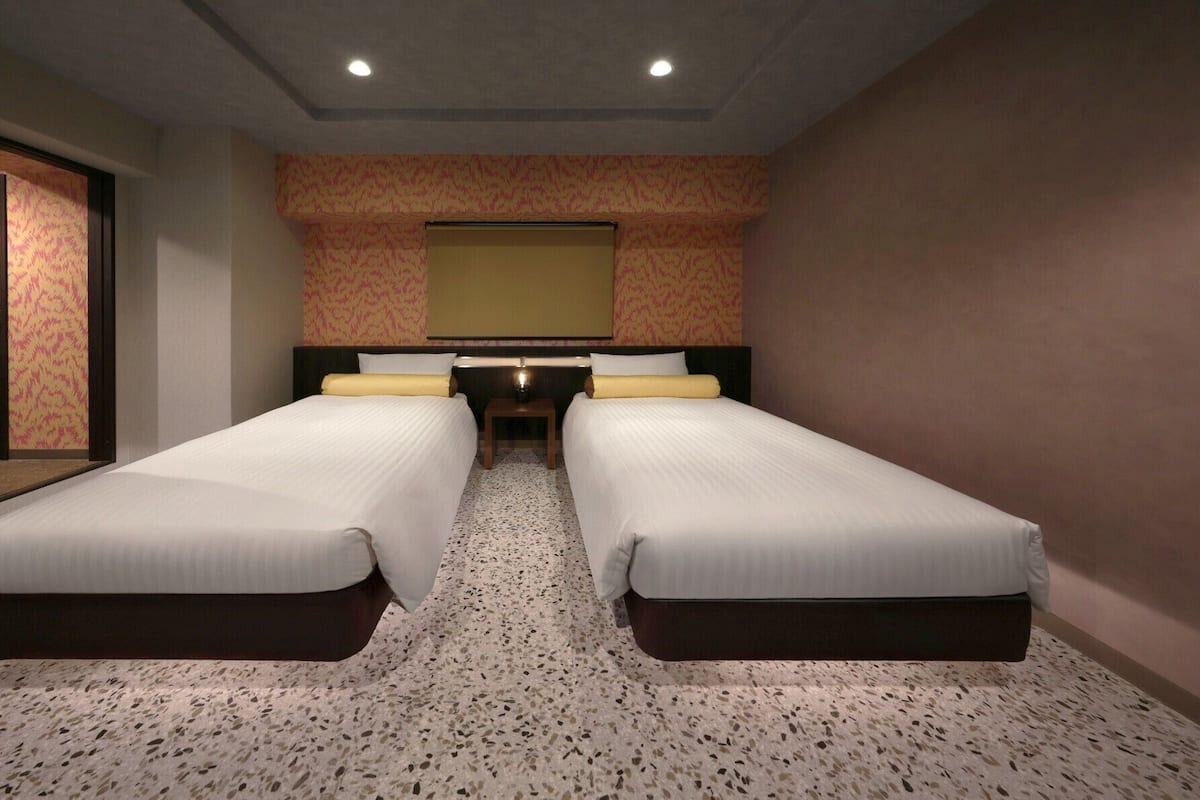 A hotel room with two beds, a small table, and a large mirror on the wall.