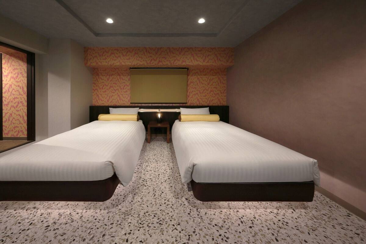 A hotel room with two beds, a small table, and a large mirror on the wall.