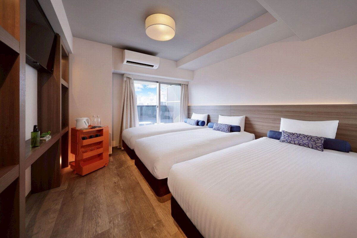 Habitación de hotel con dos camas, un cabecero de madera, una mesita con una tetera y un equipo de aire acondicionado.