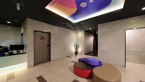 A lobby with a reception desk, a potted plant, and colorful seating areas. - Nipponbashi LUXE Hotel (Osaka)