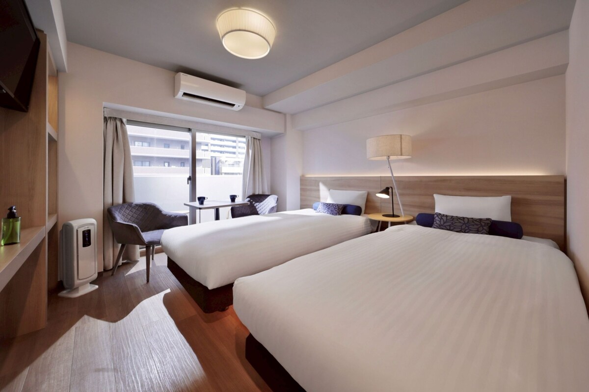 Habitación de hotel con dos camas, un escritorio, una silla, una lámpara y un equipo de aire acondicionado.