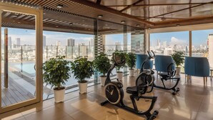 A spacious gym with exercise equipment, potted plants, and large windows offering a city view. - Mitisa Hotel Da Nang - Near Dragon Bridge (Da Nang)