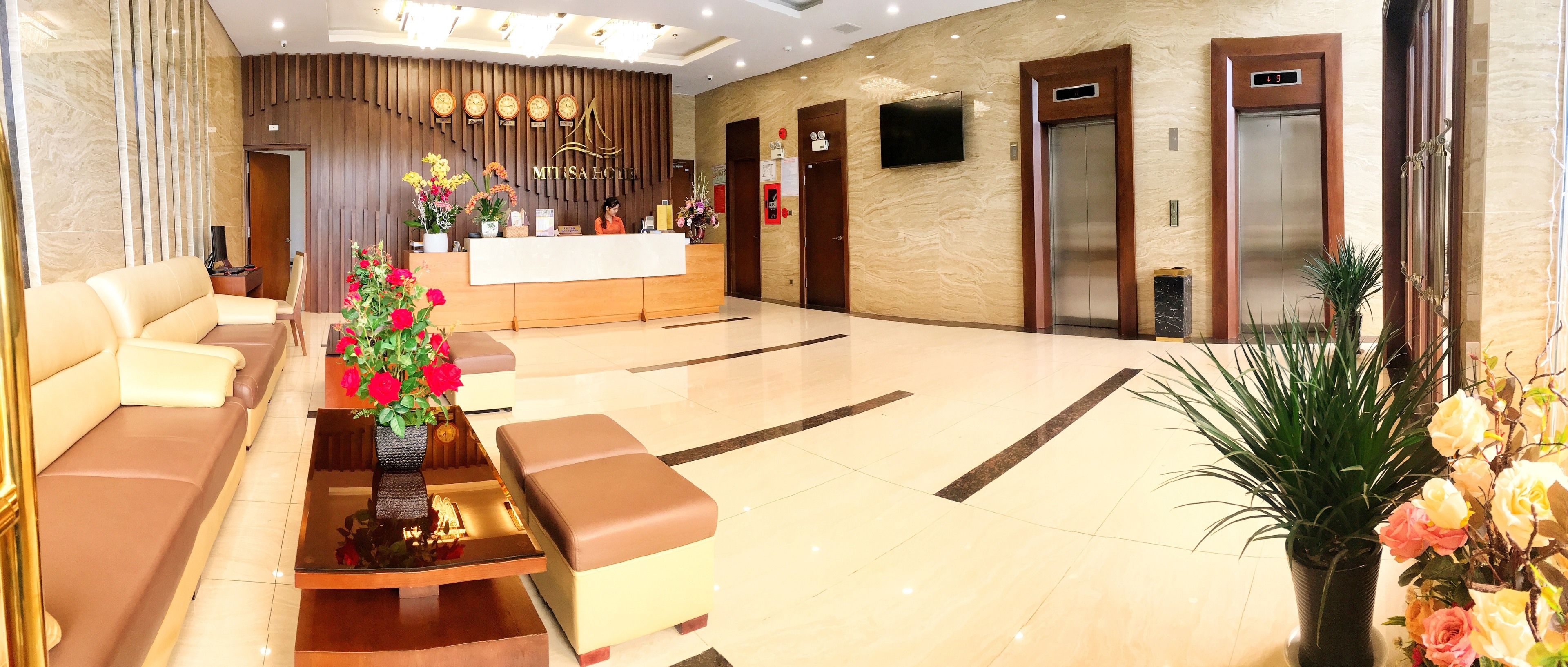 Zona de recepción de un hotel con mostrador, dos ascensores y un área de estar con sofás y una mesita de centro.