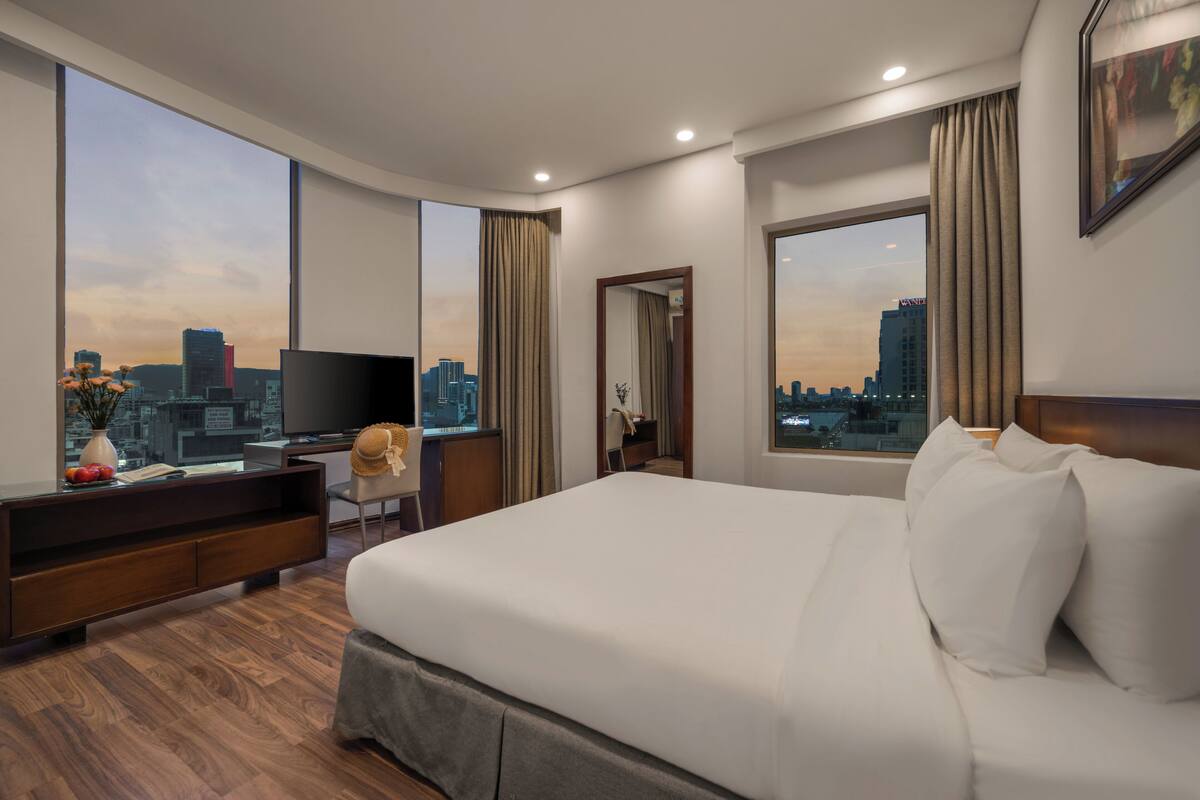 A hotel room with a large bed, a TV, a desk, and a city view.