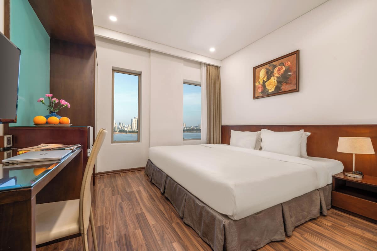 A hotel room with a large bed, a desk with a laptop, a chair, a TV, and a painting on the wall.