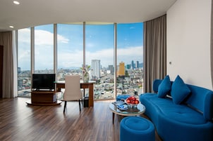 Uma sala de estar moderna com uma janela grande, um sofá azul, uma mesa de centro com frutas e uma TV sobre um suporte de madeira.