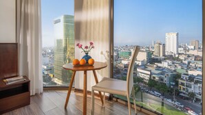 A room with a large window, a wooden table with a vase of flowers, and a chair. - Mitisa Hotel Da Nang - Near Dragon Bridge (Da Nang)