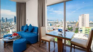 A modern hotel room with a curved sofa, a dining table, and a view of a cityscape. - Mitisa Hotel Da Nang - Near Dragon Bridge (Da Nang)