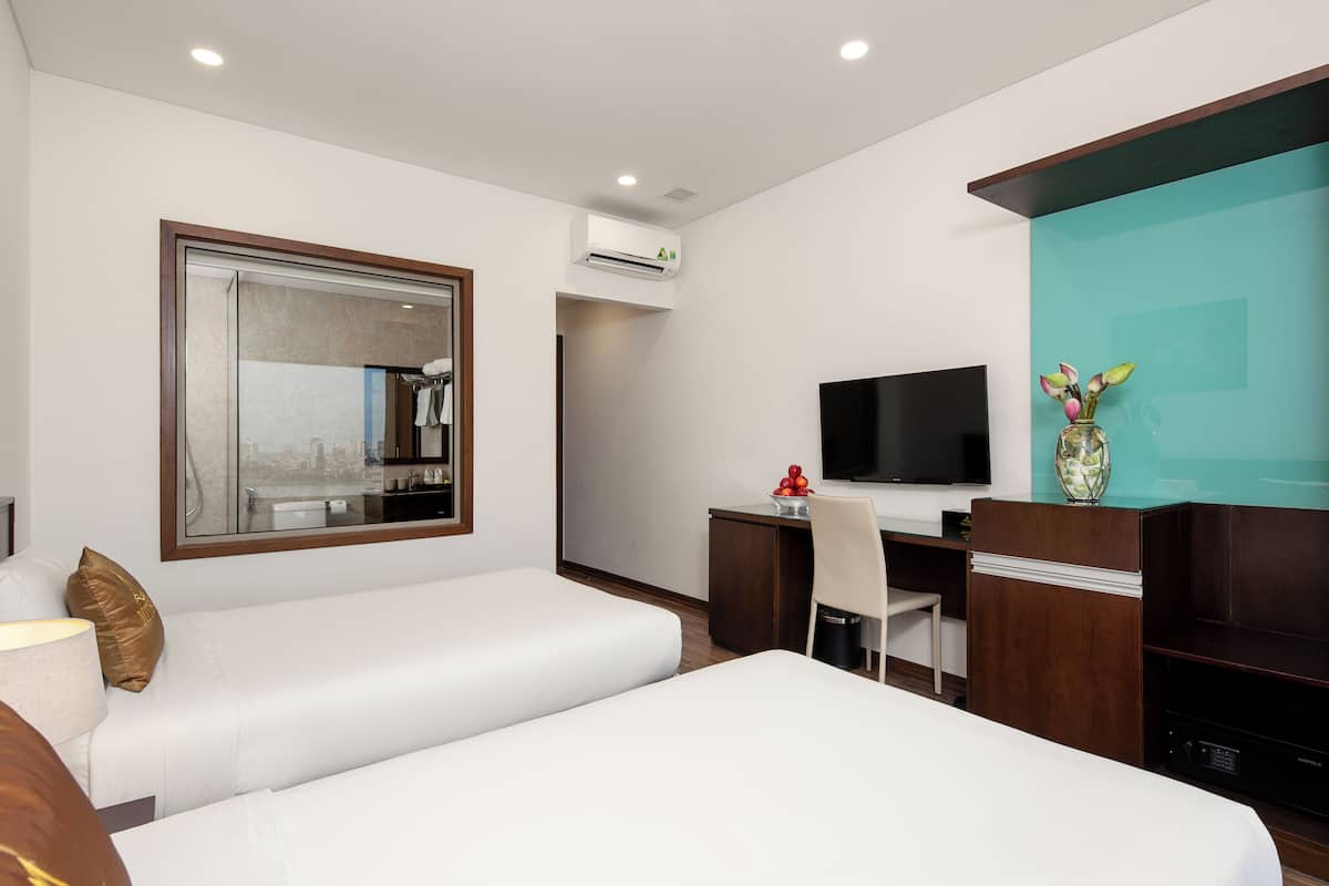 A hotel room with a large bed, a desk with a chair, a television, and a mirror.