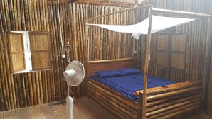 Une pièce avec un mur en bambou, un lit à baldaquin et un ventilateur sur pied.