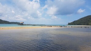 Une plage à l’eau claire, une jetée en bois et une petite cabane.