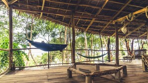 Une terrasse en bois avec un toit de chaume, un hamac et un banc.