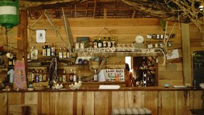 Un bar à l’ambiance rustique, avec des étagères en bois remplies de bouteilles, un menu écrit à la craie et un panneau indiquant les heures d’ouverture de la cuisine.