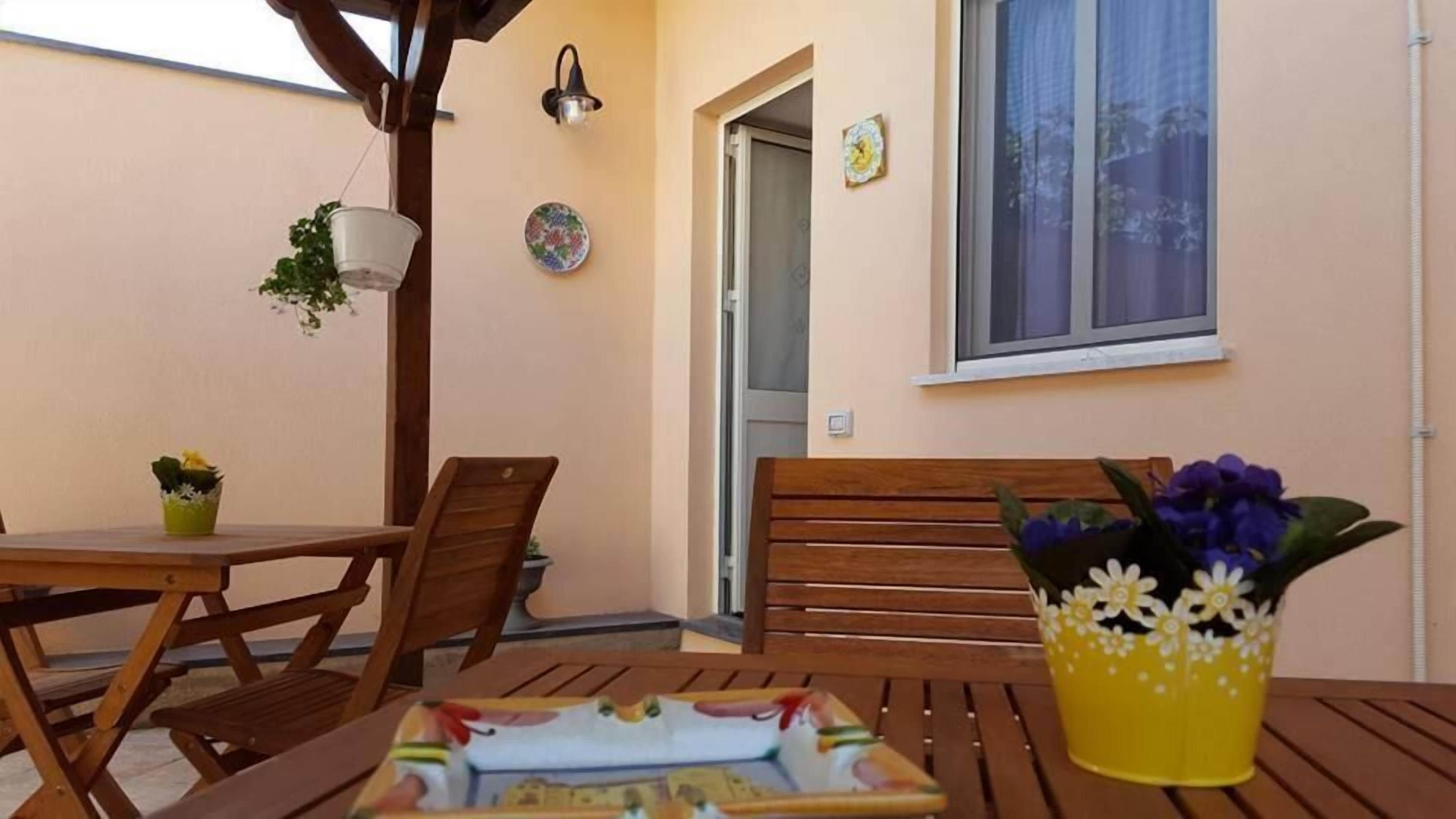 Un'area salotto all'aperto con mobili in legno, un tavolo con un piatto decorativo e un vaso giallo con fiori.