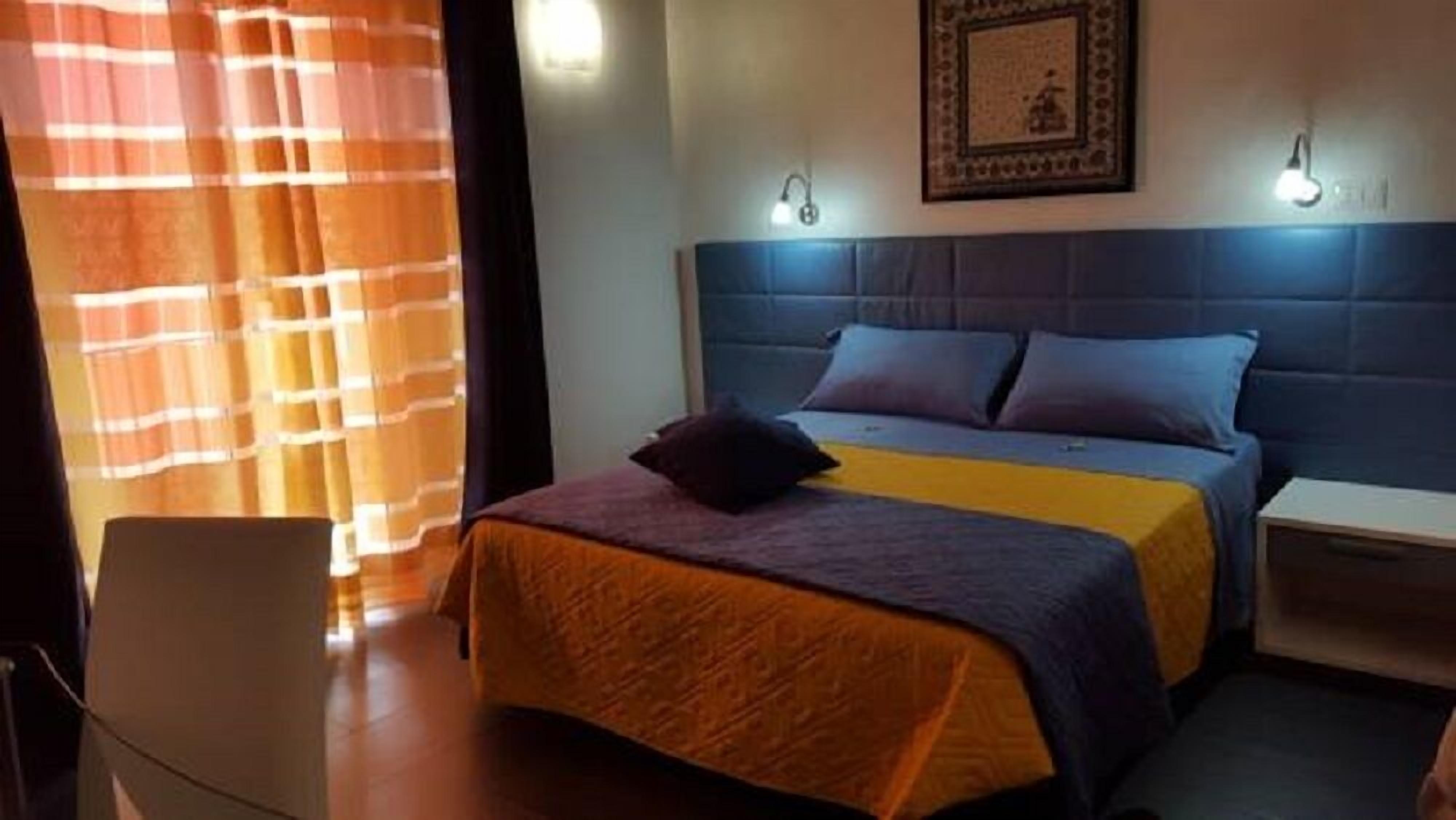 A bedroom with a bed, a bedside table, a chair, and a window with curtains.