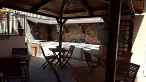 Uma área de pátio ao ar livre com parede de pedra, móveis de madeira e bancada de cozinha.