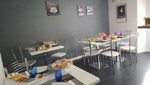 Uma área de refeições com várias mesas e cadeiras, uma parede cinza com quadros e um chão em mosaico.