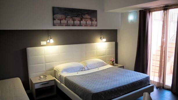 Quarto de hotel com uma cama grande, mesas de cabeceira, um criado-mudo, um quadro na parede e uma janela com cortinas.
