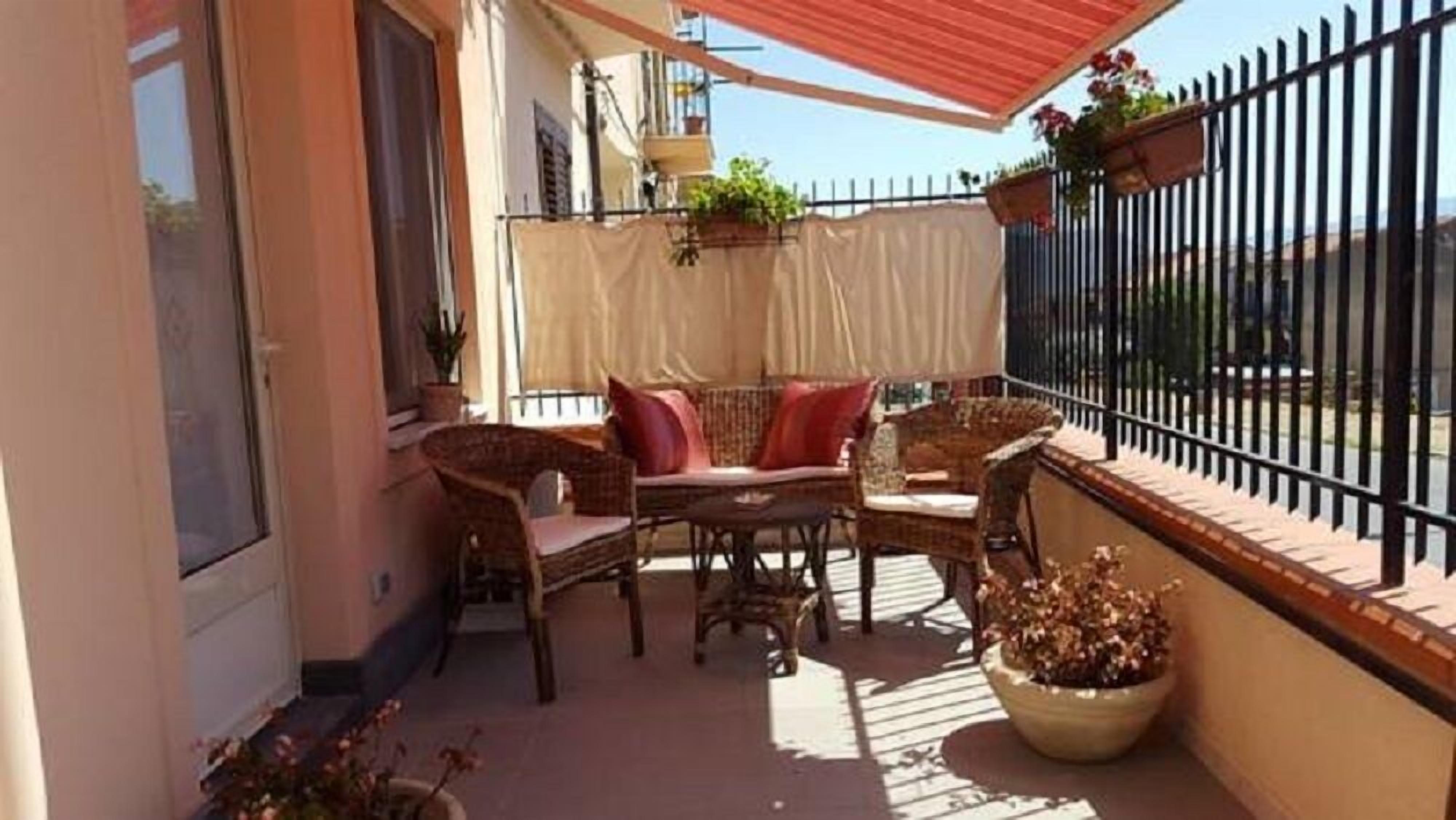 Un balcón con mobiliario de mimbre, una mesa y plantas en macetas.