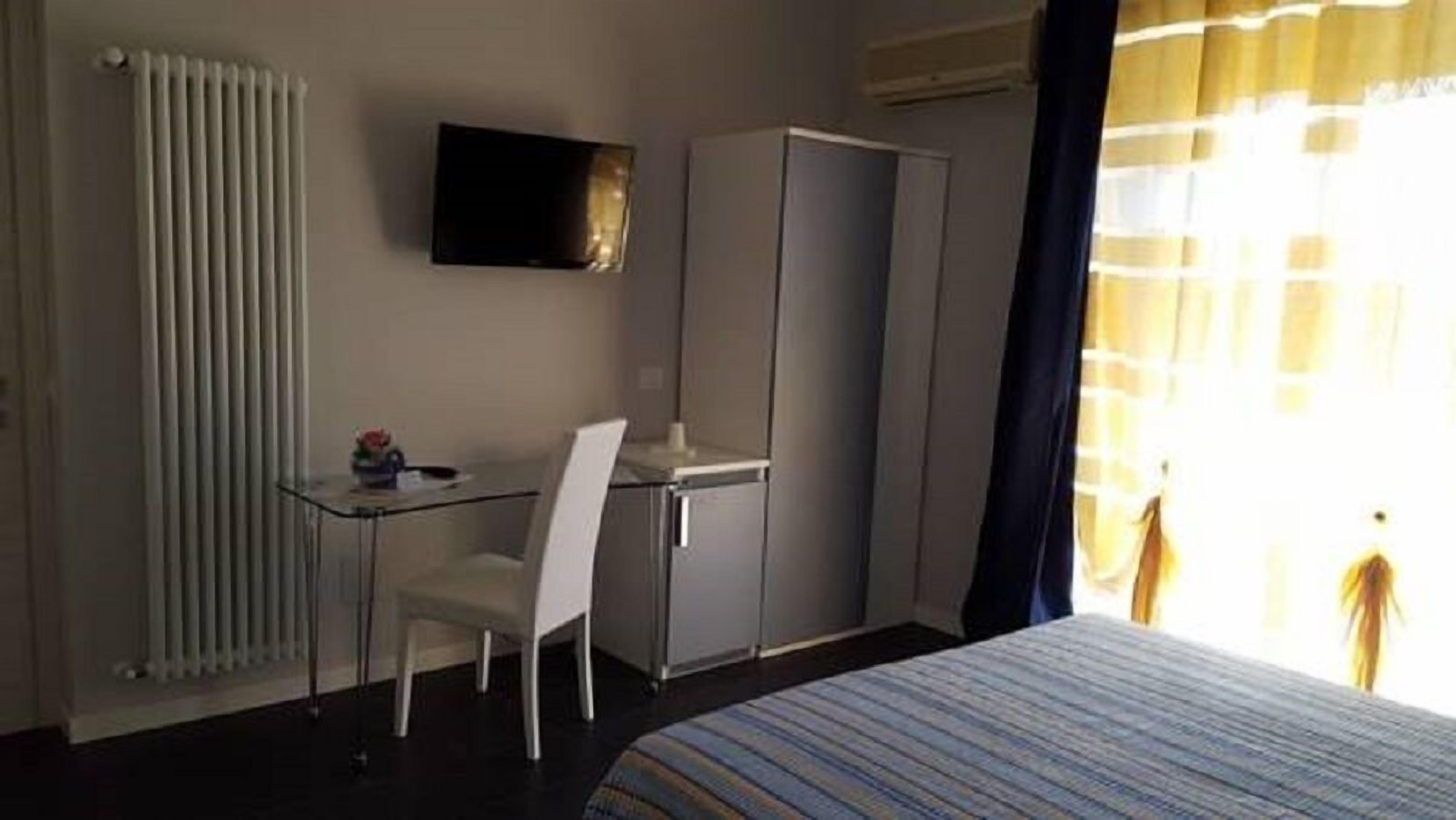 A hotel room with a bed, a desk with a chair, a television, and a radiator.