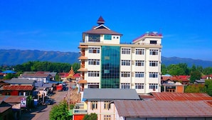 A multi-story building with a prominent glass facade, surrounded by smaller buildings and a mountainous backdrop. - Royal Inlay Hotel (Nyaungshwe)