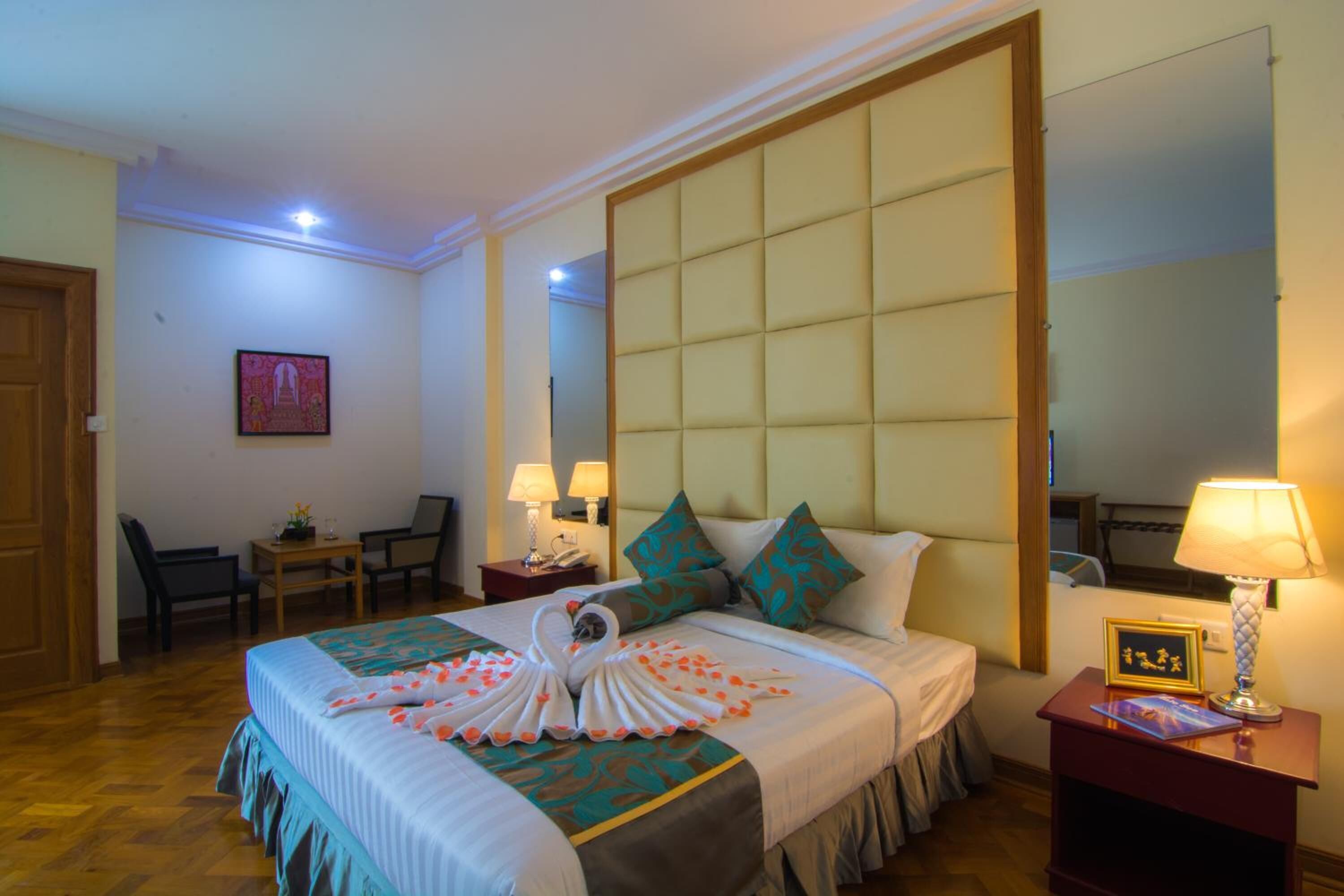 Une chambre d’hôtel avec un grand lit, un bureau, deux chaises, une table de chevet avec une lampe et un miroir.
