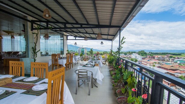 A covered outdoor dining area with tables set for two, surrounded by potted plants and overlooking a cityscape. - Royal Inlay Hotel (Nyaungshwe)