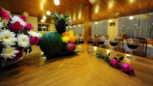 A wooden dining table with a fruit centerpiece, wine glasses, and a flower arrangement. - Royal Inlay Hotel (Nyaungshwe)