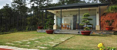 Una casa moderna con fachada de vidrio, rodeada de un jardín bien cuidado con plantas en macetas y césped.