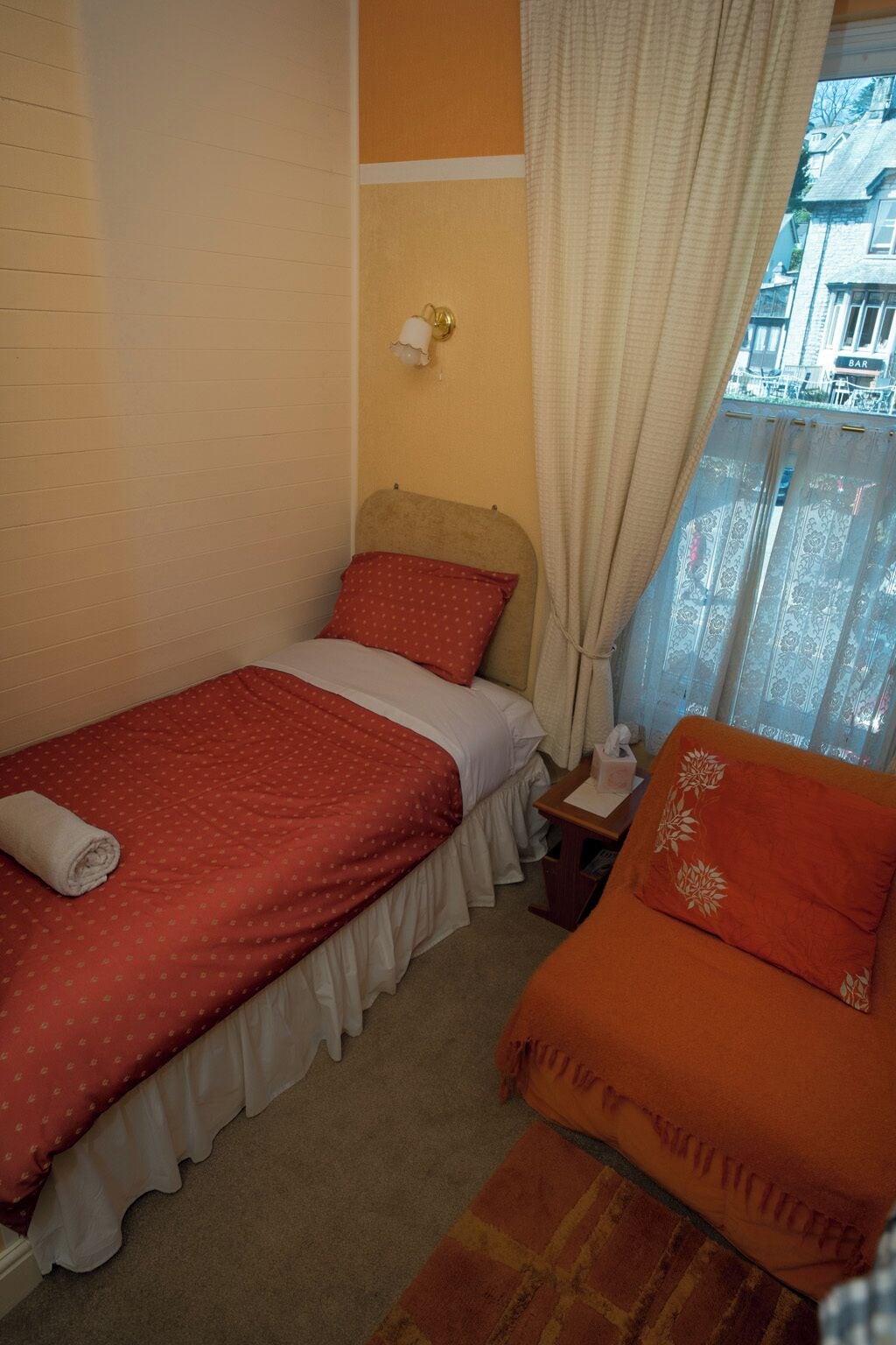 A small, cozy room with a single bed, a nightstand, and a window with curtains.
