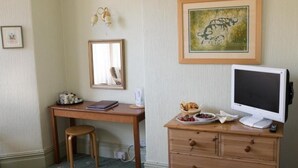 Huoneessa on työpöytä, tuoli, laatikoilla varustettu lipasto, televisio, seinällä oleva kehystetty kuva sekä pieni pöytä, jonka päällä on kori ja hedelmävati.
