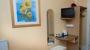 Huoneessa on kehystetty auringonkukkatyö, peili, hyllyllä oleva televisio, pieni valkoinen penkki ja patteri.