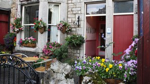 A stone building with a sign reading "Somerset House." There are outdoor seating areas with tables and chairs, and flower baskets hanging on the windows. - Somerset House (Grange-over-Sands)