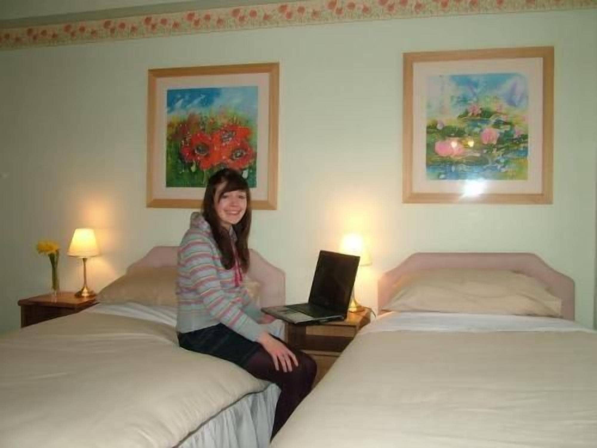 Ein Zimmer mit zwei Betten, einem Laptop auf einem Nachttisch und zwei Lampen.