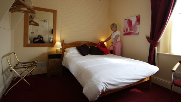 A bedroom with a wooden bed, a mirror, a hanging chair, and a window with curtains. - Somerset House (Grange-over-Sands)