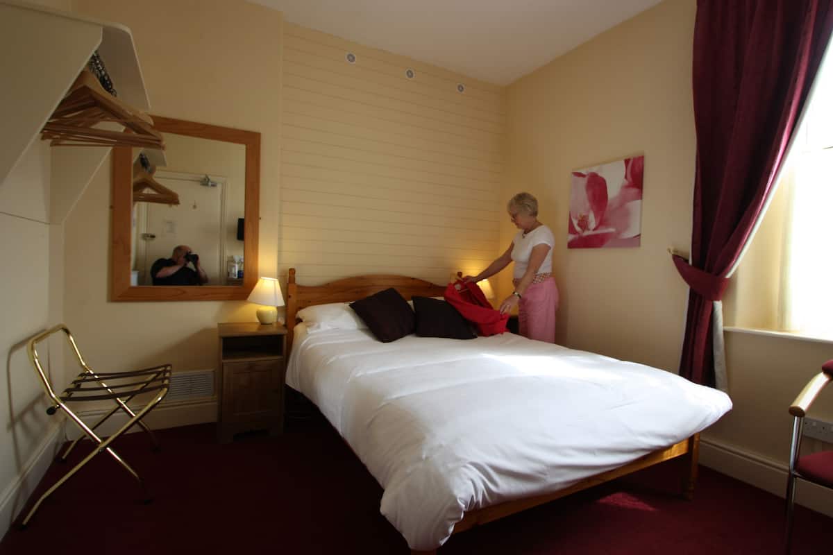 A bedroom with a wooden bed, a mirror, a hanging chair, and a window with curtains.