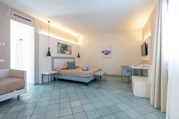 A modern hotel room with a bed, bedside table, chair, desk, and a TV.