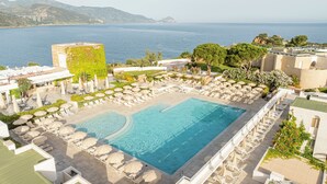 Zona de piscina con múltiples tumbonas y sombrillas, rodeada de vegetación y con vista a un cuerpo de agua.
