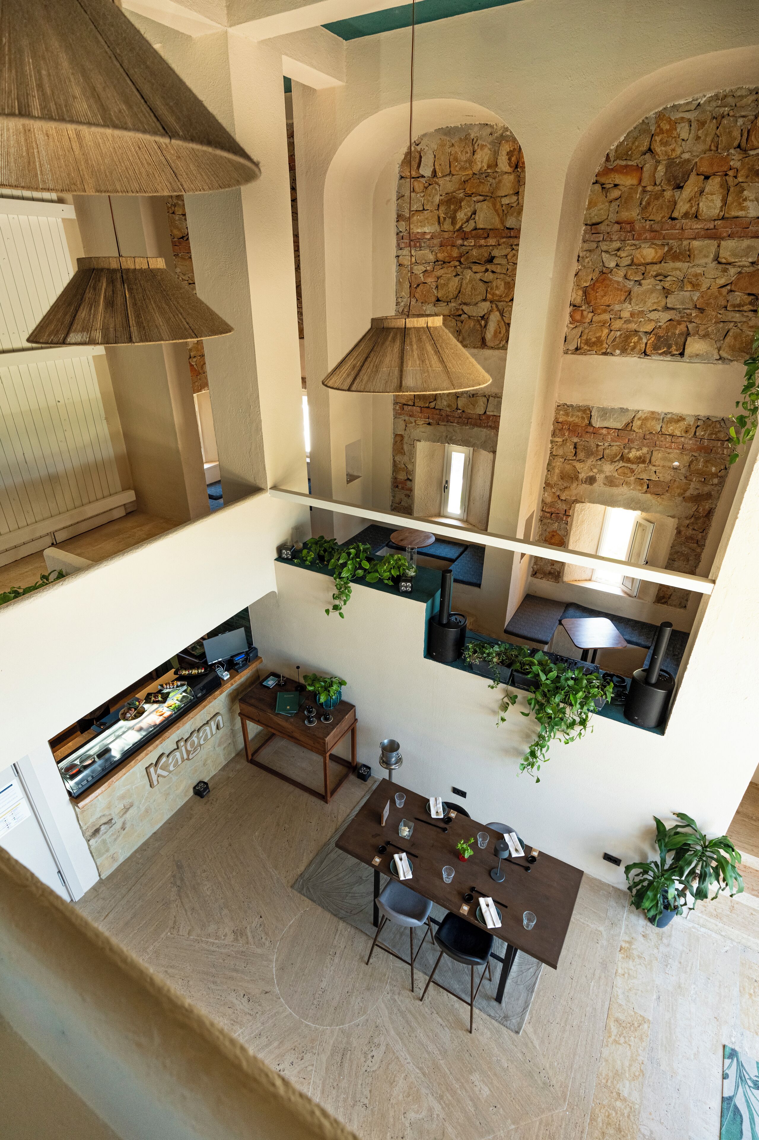 A modern loft-style dining area with a high ceiling, exposed stone walls, and hanging pendant lights.