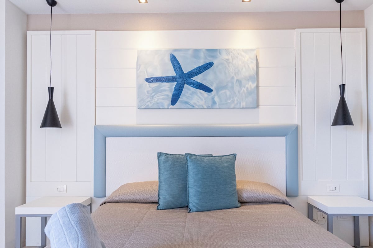 A modern bedroom with a large bed, two bedside tables, a wall-mounted artwork, and a ceiling light fixture.