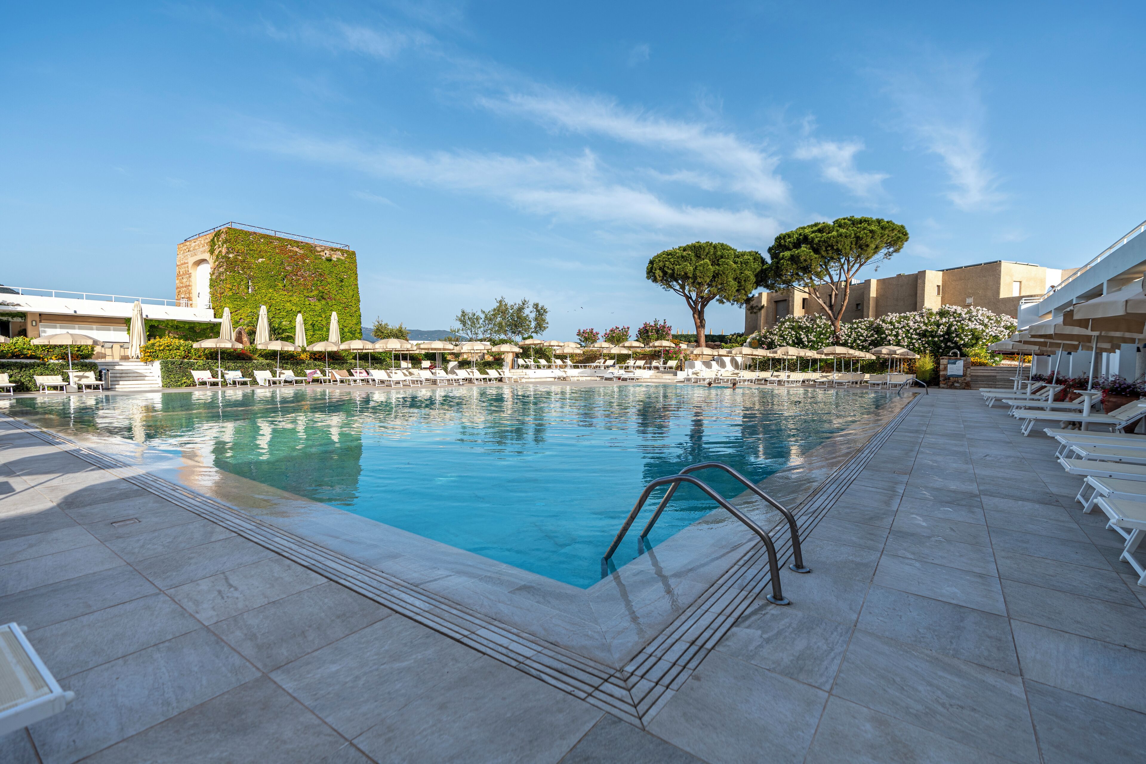 Ein Pool mit Liegestühlen und Sonnenschirmen, umgeben von Gebäuden mit einer gefliesten Terrasse.