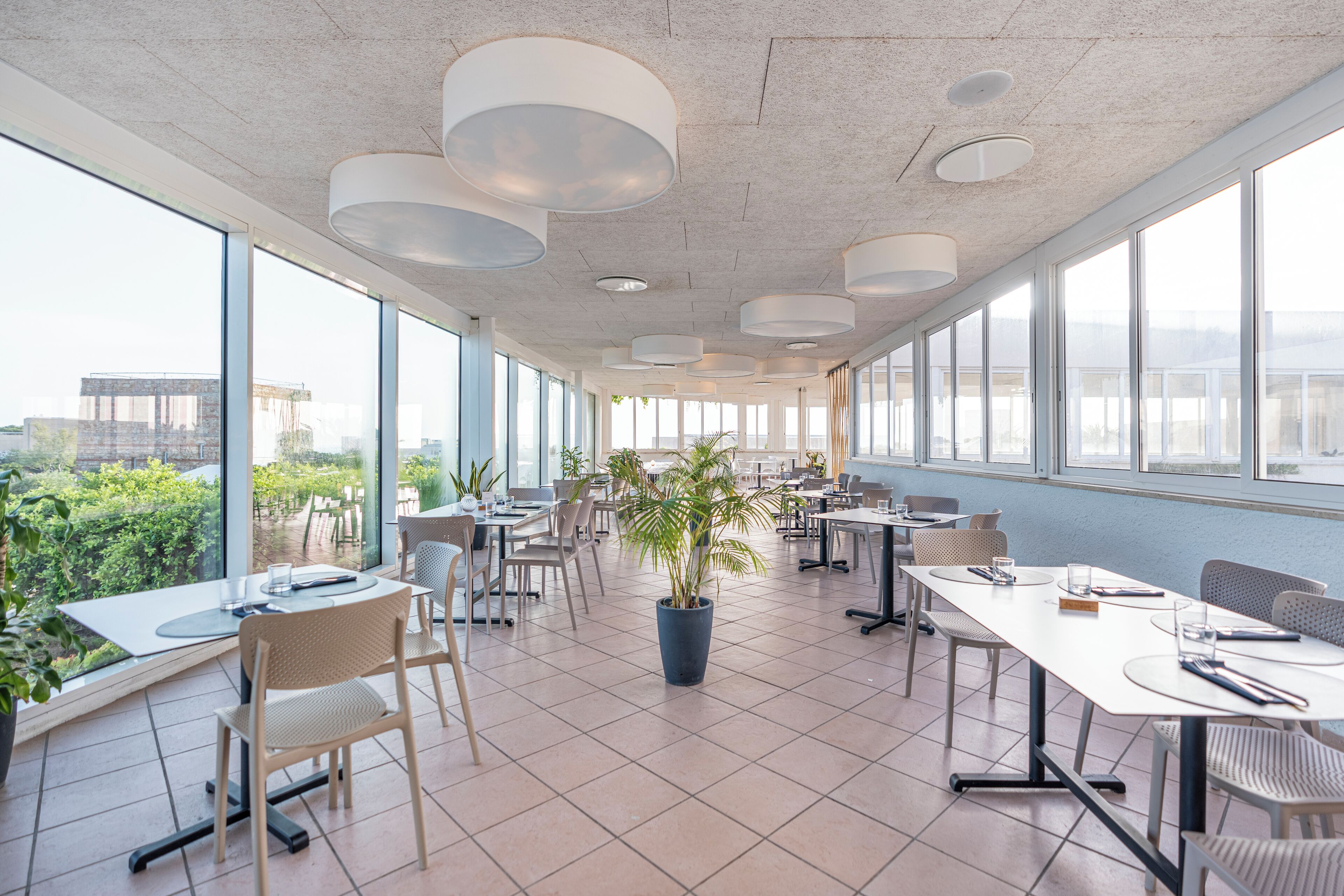 A spacious conference room with large windows, modern lighting fixtures, and a potted plant.