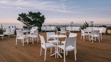Una terraza con mobiliario exterior blanco, incluyendo mesas y sillas, con vista a un cuerpo de agua.