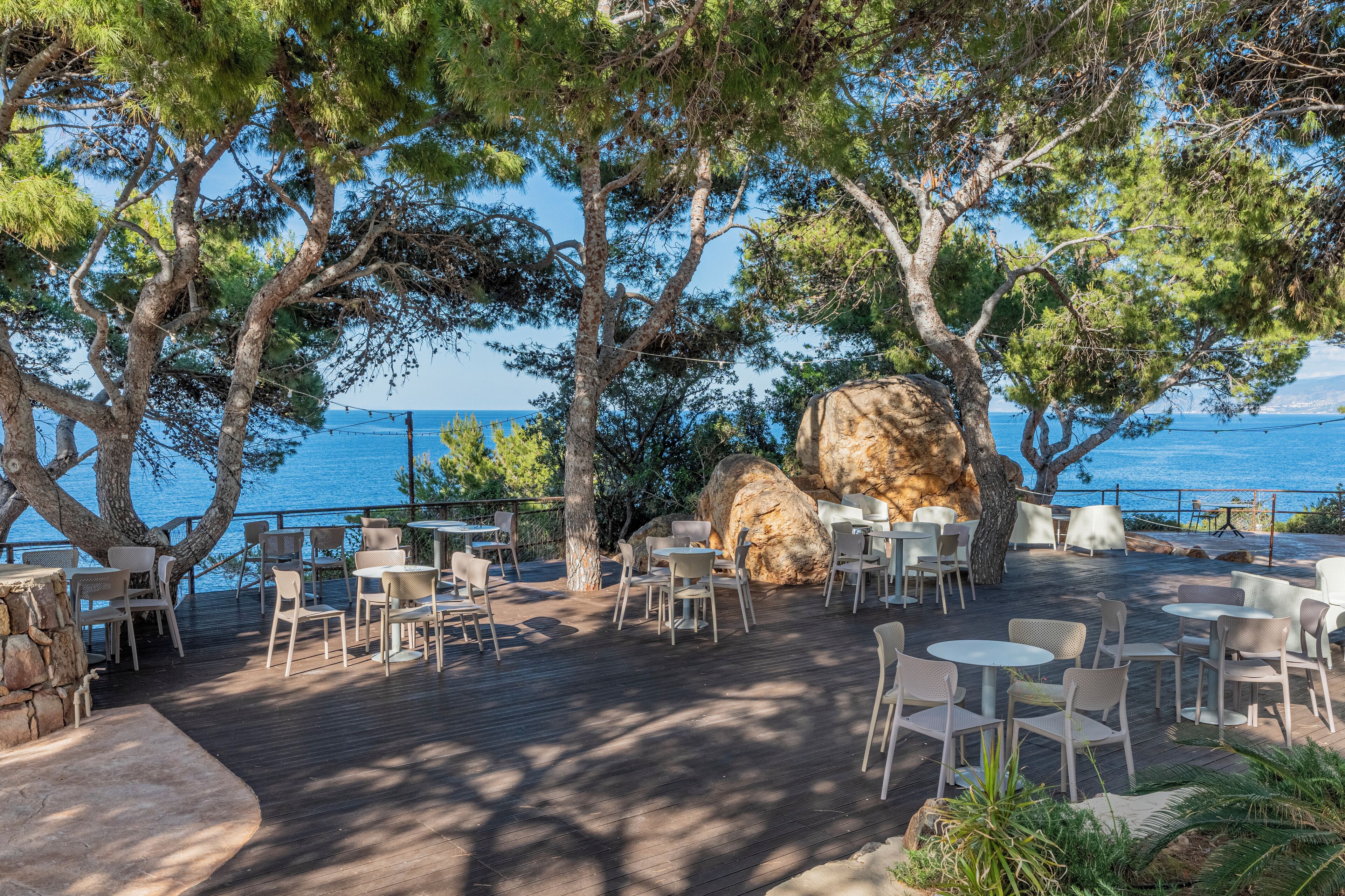 An outdoor seating area with tables and chairs, overlooking a body of water.