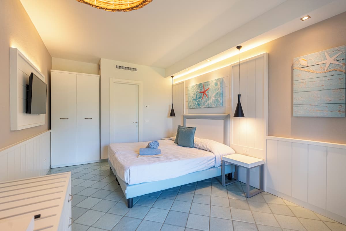 A bedroom with a bed, bedside tables, a TV, and artwork on the walls.