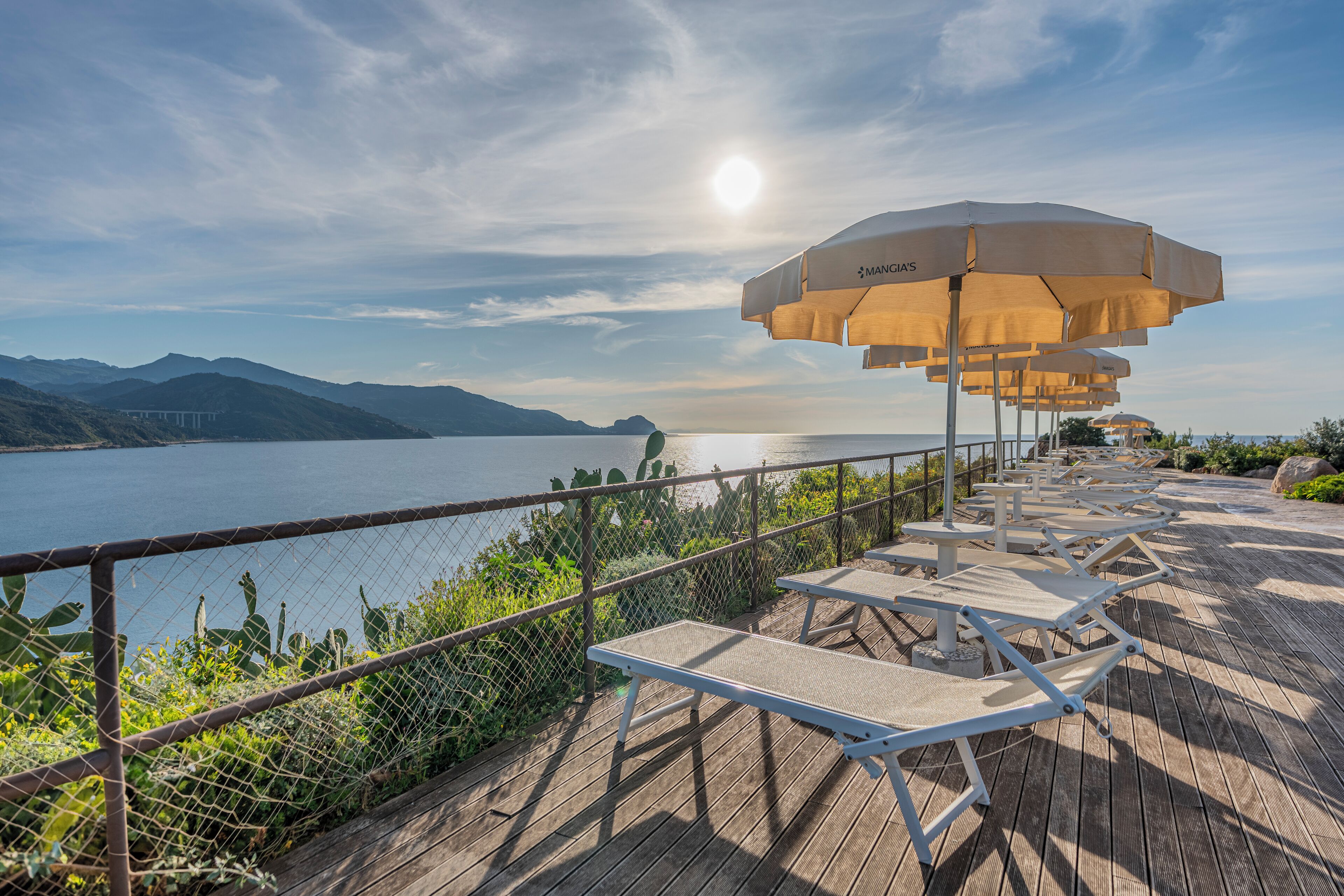 A deck with lounge chairs and umbrellas overlooking a lake with mountains in the background.
