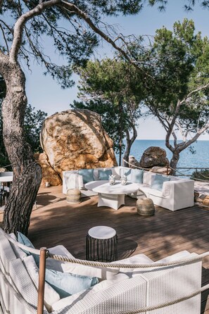 An outdoor seating area with wicker furniture, a round table, and a view of the sea.
