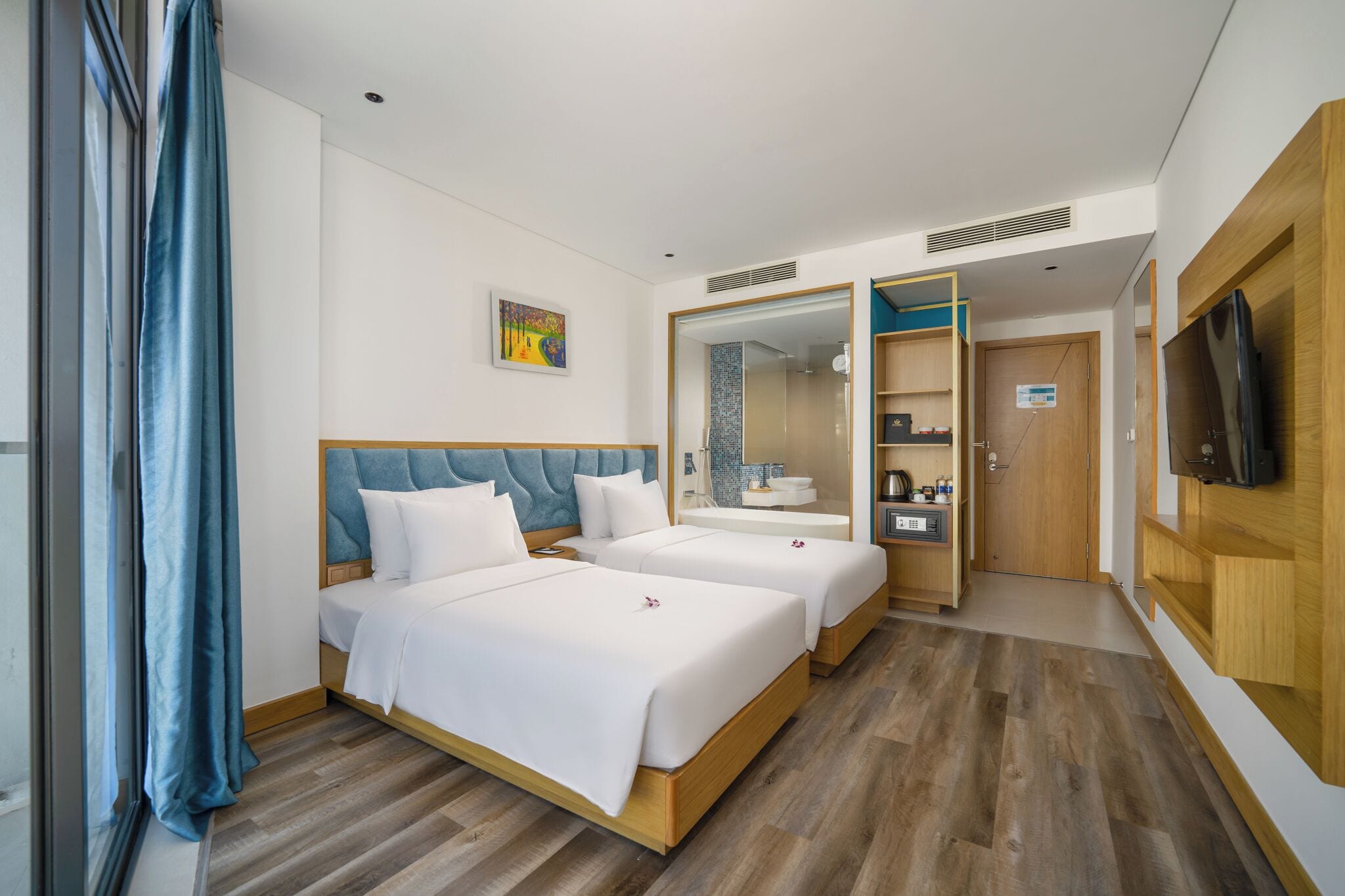 Habitación de hotel con dos camas, baño, televisor y armario de madera.